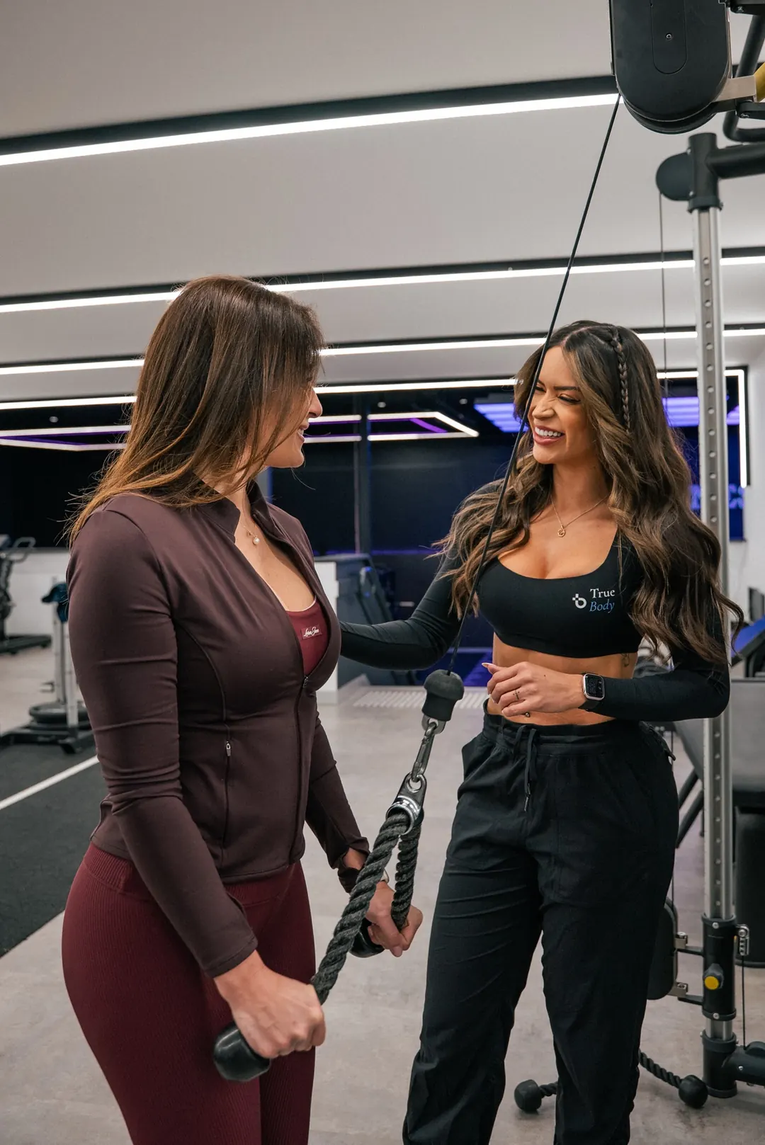 True Body trainer Bruna Tavares coaching a client at the cable machine.